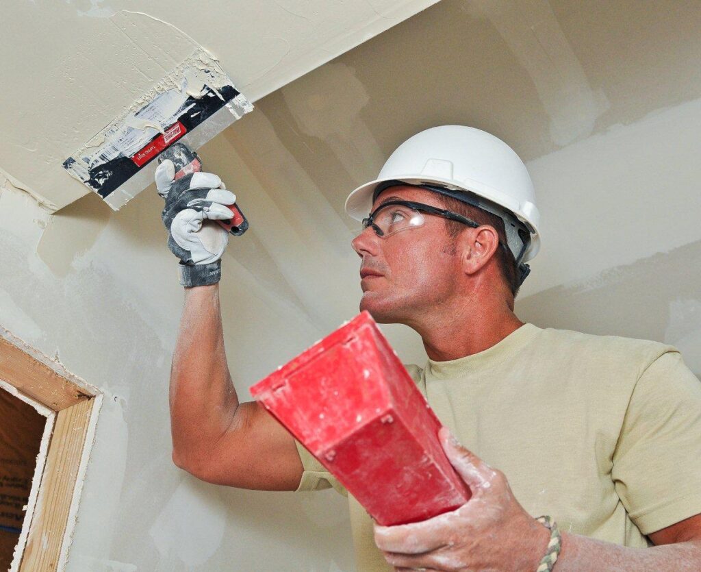 Worker applying joint compound to a drywall ceiling seam