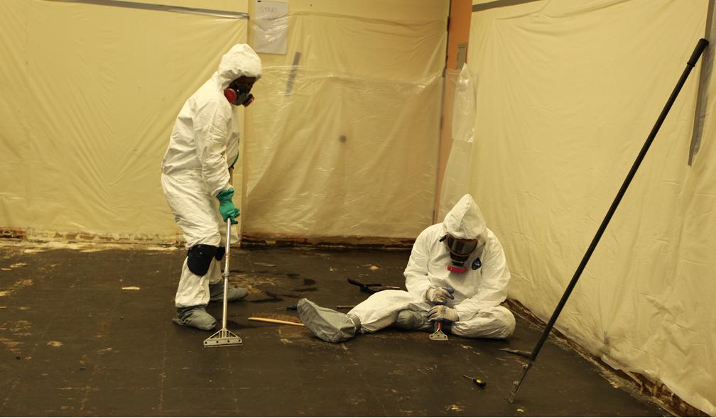 Workers in protective equipment carrying out flooring abatement in a contained room